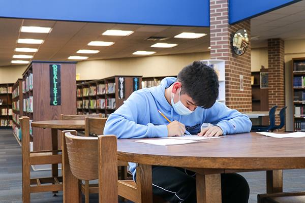 high school student works on homework in library